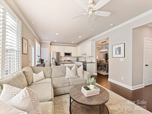 living room with recessed lighting, ornamental molding, ceiling fan with notable chandelier, baseboards, and dark wood-type flooring
