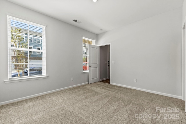 carpeted empty room featuring plenty of natural light, visible vents, and baseboards