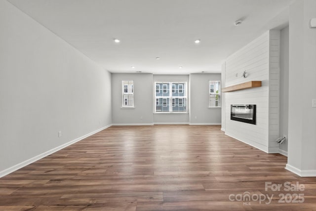 unfurnished living room with a large fireplace, baseboards, recessed lighting, and dark wood-type flooring