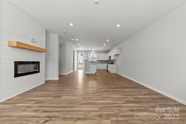 unfurnished living room with a large fireplace, baseboards, recessed lighting, and wood finished floors