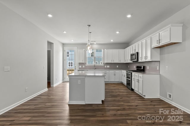 kitchen with dark wood-type flooring, white cabinets, a kitchen island, appliances with stainless steel finishes, and decorative backsplash