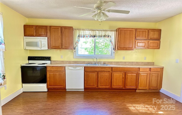 kitchen with white appliances, brown cabinetry, dark wood-style flooring, light countertops, and a sink