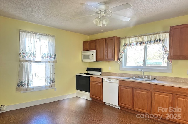 kitchen featuring white appliances, brown cabinetry, a textured ceiling, dark wood-style flooring, and a sink
