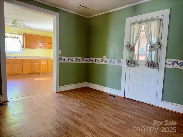 spare room with light wood-type flooring, crown molding, a ceiling fan, visible vents, and a sink