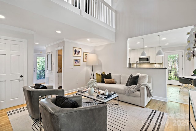 living area featuring recessed lighting, baseboards, ornamental molding, and light wood-style flooring
