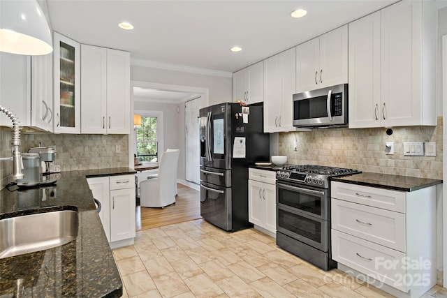 kitchen featuring appliances with stainless steel finishes, tasteful backsplash, glass insert cabinets, ornamental molding, and white cabinetry