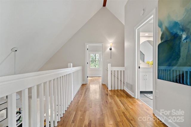 hall featuring light wood-type flooring, vaulted ceiling, an upstairs landing, and visible vents