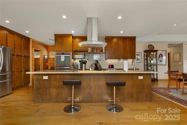 263 Mine Cove Rd, Spruce Pine, NC 28777 - kitchen with island range hood, light stone counters, a breakfast bar, appliances with stainless steel finishes, and light wood-type flooring
