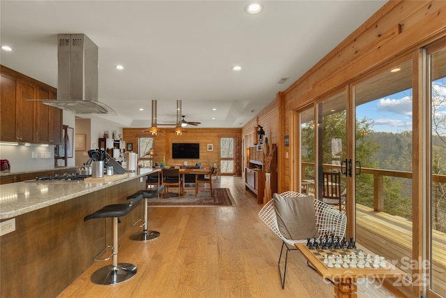 263 Mine Cove Rd, Spruce Pine, NC 28777 - kitchen with light wood-style floors, island exhaust hood, a kitchen bar, a ceiling fan, and wood walls