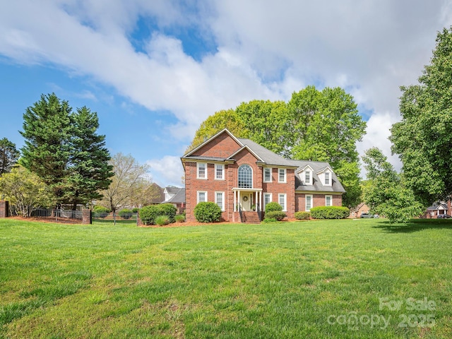 colonial-style house featuring a front yard, brick siding, and fence