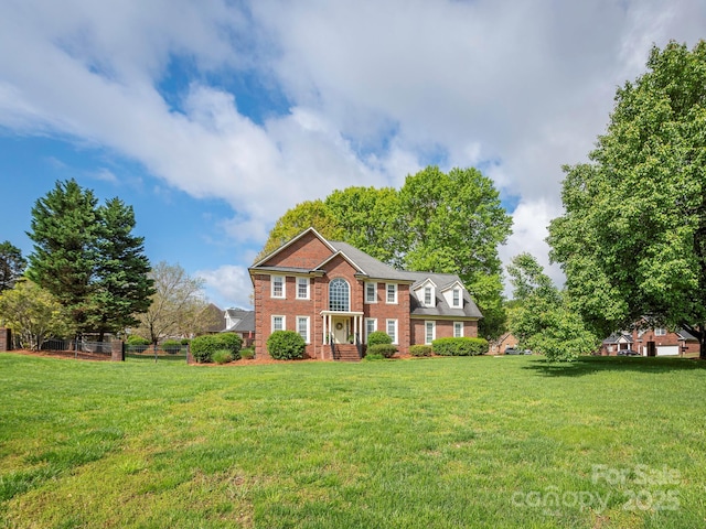 colonial home with fence, a front lawn, and brick siding