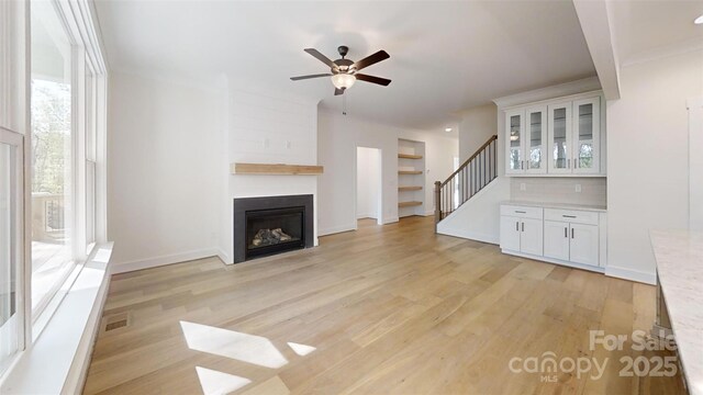 472 Bellingshire Dr, Mount Ulla, NC 28125 - unfurnished living room featuring ceiling fan, a glass covered fireplace, visible vents, stairs, and light wood finished floors