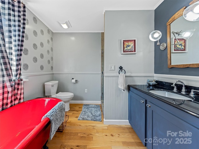 bathroom featuring vanity, ornamental molding, toilet, wood finished floors, and wainscoting