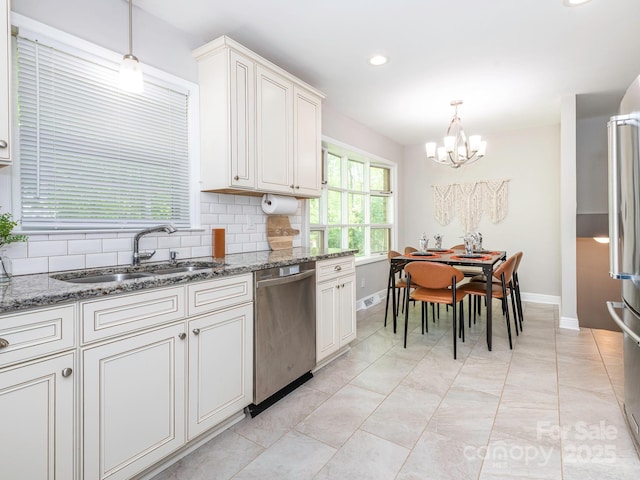kitchen featuring a sink, appliances with stainless steel finishes, a chandelier, light stone countertops, and backsplash