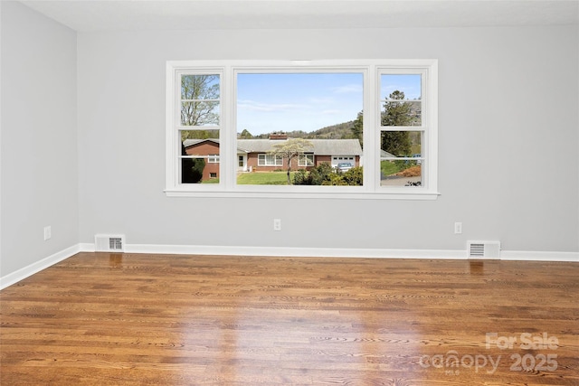 empty room featuring visible vents, baseboards, and wood finished floors