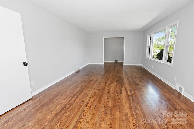 empty room with dark wood-style flooring, baseboards, and visible vents