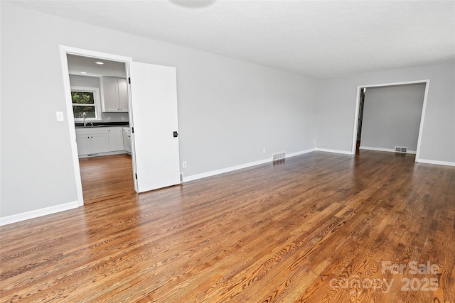 unfurnished room with a sink, baseboards, dark wood finished floors, and visible vents