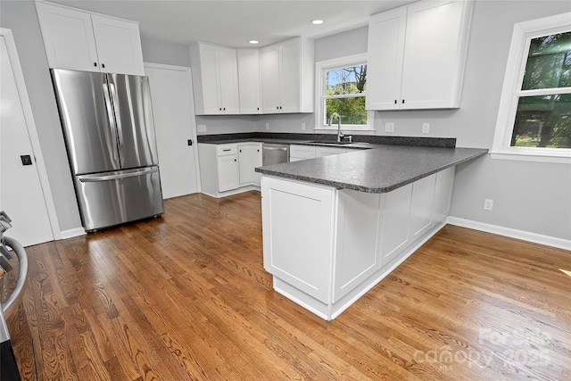 kitchen with a peninsula, white cabinetry, dark countertops, appliances with stainless steel finishes, and a sink