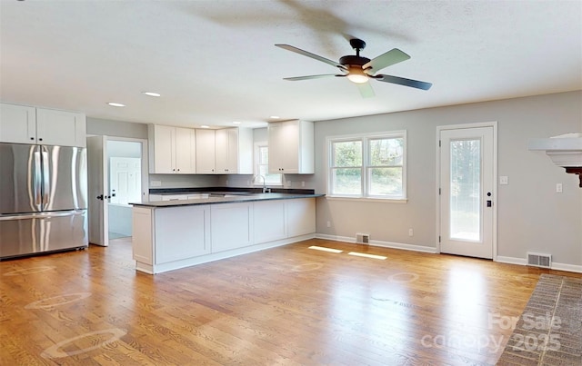 kitchen with a peninsula, dark countertops, stainless steel fridge, and visible vents