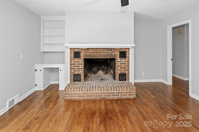 unfurnished living room featuring a brick fireplace, visible vents, and wood finished floors