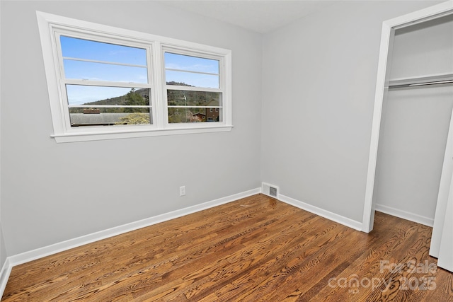 unfurnished bedroom with visible vents, a closet, baseboards, and wood finished floors