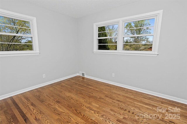 empty room featuring plenty of natural light, visible vents, baseboards, and dark wood-style floors