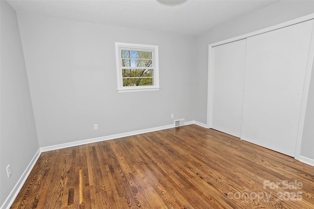 unfurnished bedroom featuring visible vents, a closet, baseboards, and wood finished floors
