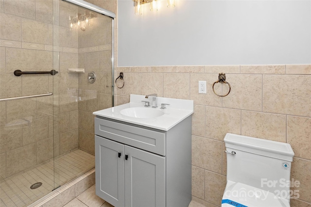 full bathroom featuring a shower stall, vanity, a wainscoted wall, toilet, and tile walls