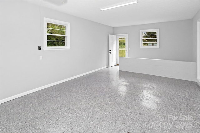 unfurnished room featuring baseboards, speckled floor, and a healthy amount of sunlight