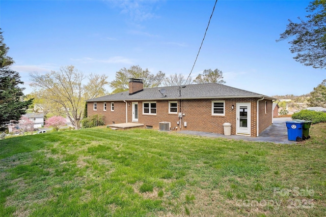 back of house featuring brick siding, central AC, a chimney, and a lawn