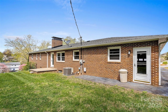 rear view of house with roof with shingles, a chimney, brick siding, central AC unit, and a lawn