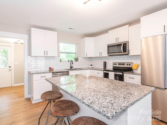 kitchen with stainless steel appliances, a sink, a kitchen bar, a center island, and tasteful backsplash