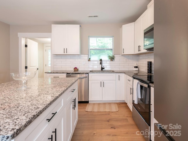 kitchen featuring stainless steel appliances, a sink, light wood-style flooring, decorative backsplash, and white cabinets