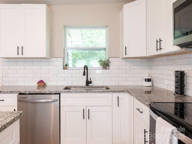 kitchen with appliances with stainless steel finishes, a sink, white cabinets, and light stone counters