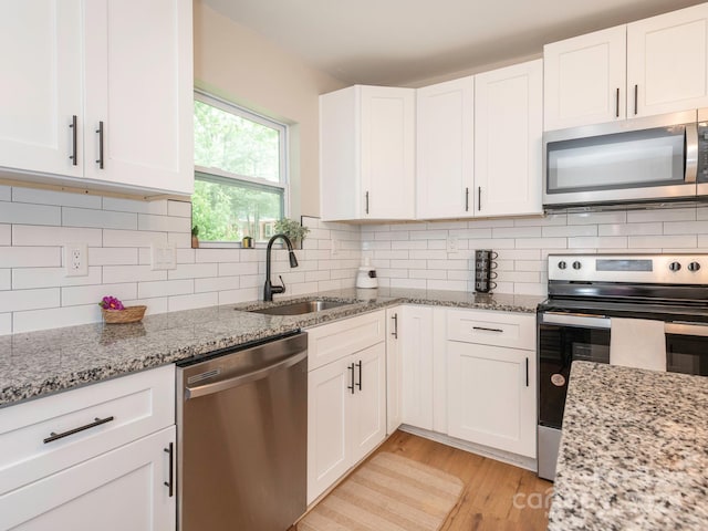 kitchen with appliances with stainless steel finishes, a sink, white cabinetry, light wood-style floors, and decorative backsplash