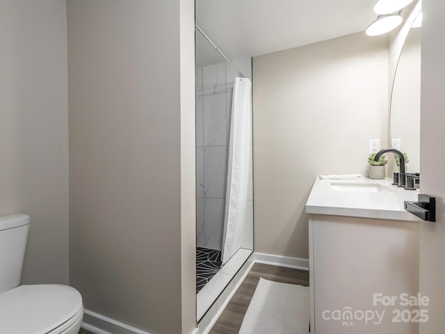 bathroom featuring toilet, a stall shower, wood finished floors, vanity, and baseboards