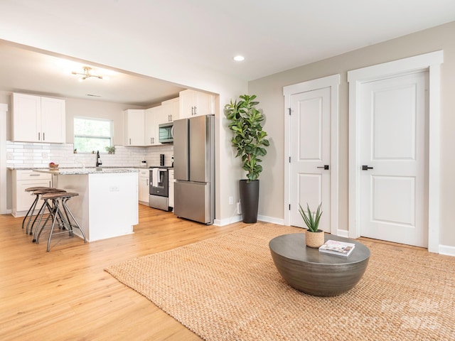 kitchen with appliances with stainless steel finishes, tasteful backsplash, white cabinets, a kitchen breakfast bar, and light wood finished floors