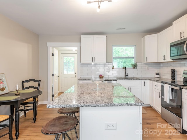 kitchen featuring appliances with stainless steel finishes, a sink, a breakfast bar, light wood-style flooring, and decorative backsplash