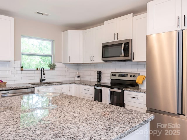 kitchen featuring appliances with stainless steel finishes, a sink, decorative backsplash, and white cabinets
