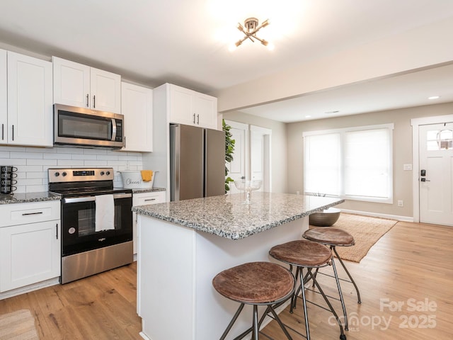 kitchen with stainless steel appliances, a kitchen breakfast bar, light stone countertops, and white cabinetry