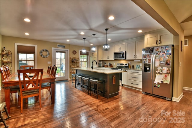 kitchen featuring appliances with stainless steel finishes, a breakfast bar, recessed lighting, dark wood-style flooring, and a center island with sink