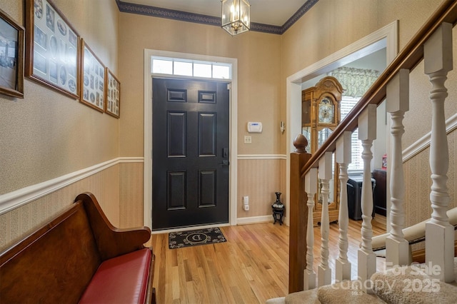 foyer with ornamental molding, stairway, wood finished floors, wallpapered walls, and a wainscoted wall
