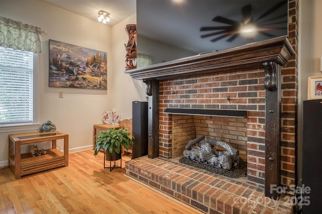 living area with wood finished floors, a fireplace, a ceiling fan, and baseboards