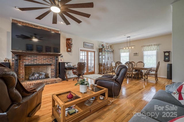 living room featuring light wood finished floors, a brick fireplace, baseboards, and ceiling fan