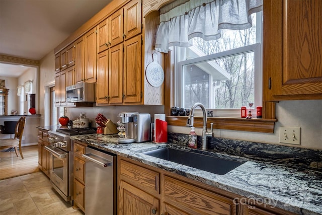 kitchen featuring a sink, appliances with stainless steel finishes, brown cabinets, stone counters, and light tile patterned flooring