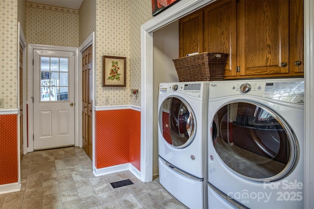 clothes washing area featuring visible vents, a wainscoted wall, wallpapered walls, cabinet space, and washer and clothes dryer