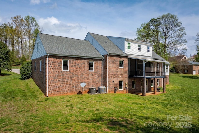 rear view of property with central AC unit, brick siding, a sunroom, and a lawn