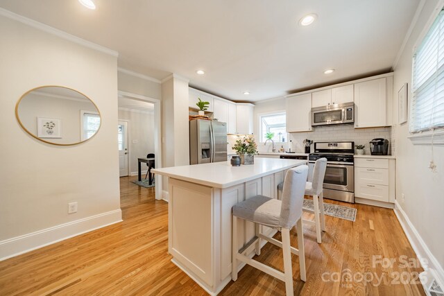 3510 Conway Ave, Charlotte, NC 28209 - kitchen featuring stainless steel appliances, decorative backsplash, white cabinets, a breakfast bar, and crown molding