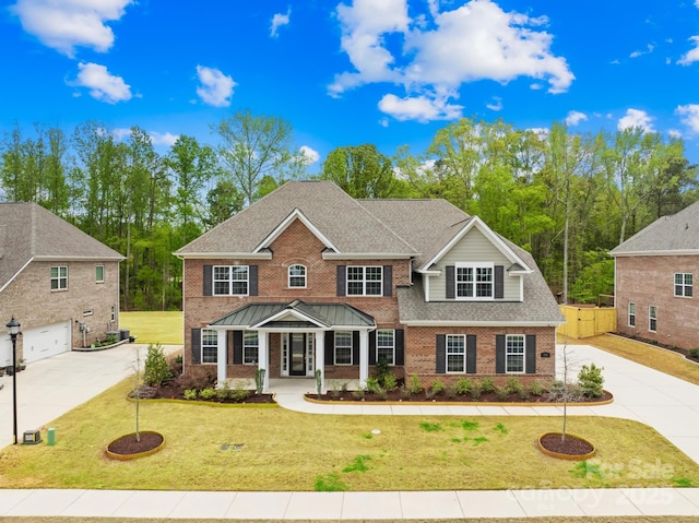 view of front of house with roof with shingles, driveway, a front yard, brick siding, and fence