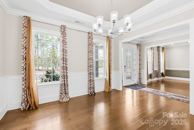empty room featuring a chandelier, visible vents, crown molding, and wood finished floors